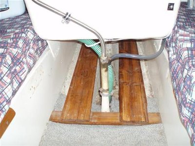 This is the area under the step. Wooden rails support the slide out stowage bucket. The clear hose is the water hose leading to a pump in the port cockpit locker. The reinforced hose is the bilge pump suction leading to the bilge pump in the starboard cockpit locker.